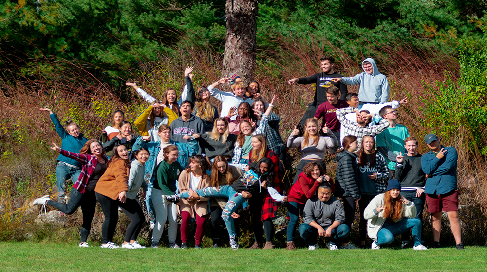 a group of students huddled together posing in the grass 