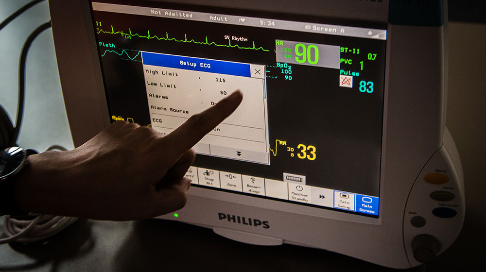 An unseen person points to a biomedical engineering cardiograph.