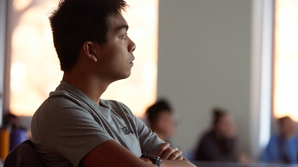 An engineering student with arms crossed, listens attentively.