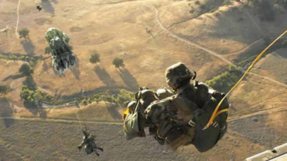 Military personnel in full uniform and gear jump out of a airplane for a training on parachute jumping for airborne school.