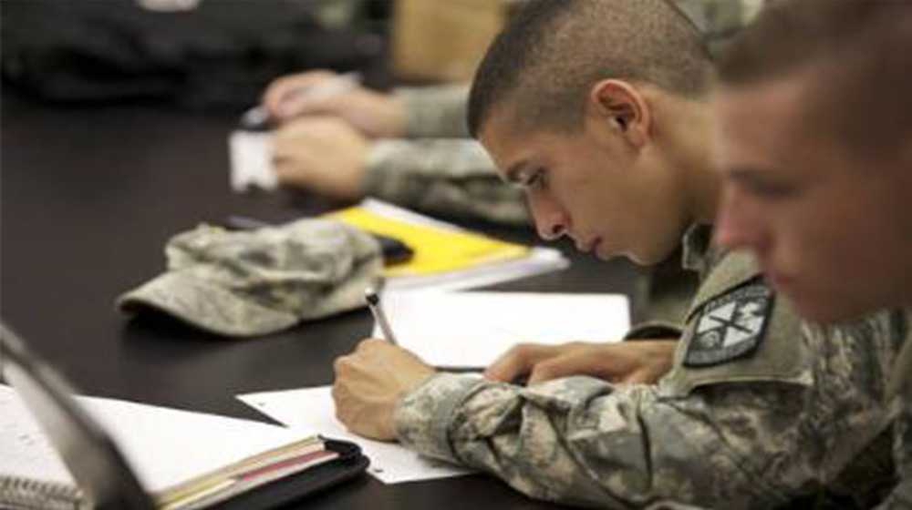 A Loyola University Chicago ROTC student writing on a piece of paper in a classroom with other students