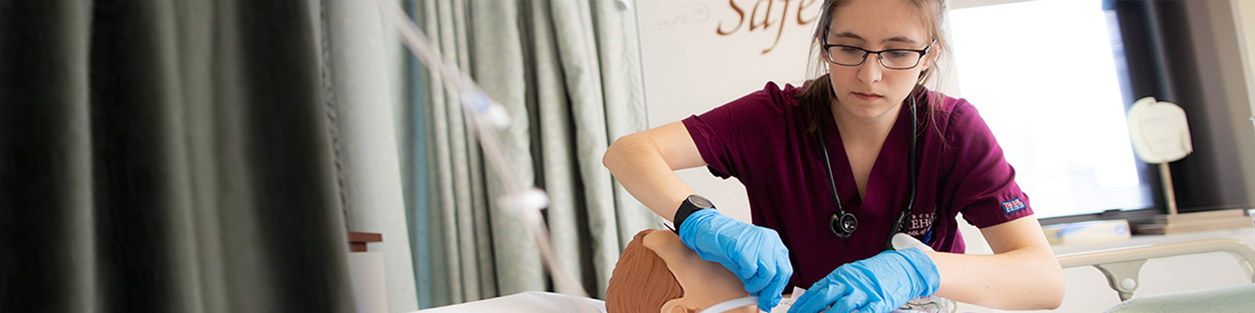 A Loyola University Chicago nursing student wearing maroon scrubs and blue gloves practices a procedure on a plastic training dummy.