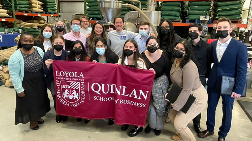 A group of students in a factory holding a Quinlan banner