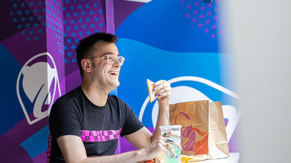 Alex Minton sitting and smiling inside a Taco Bell, eating a meal