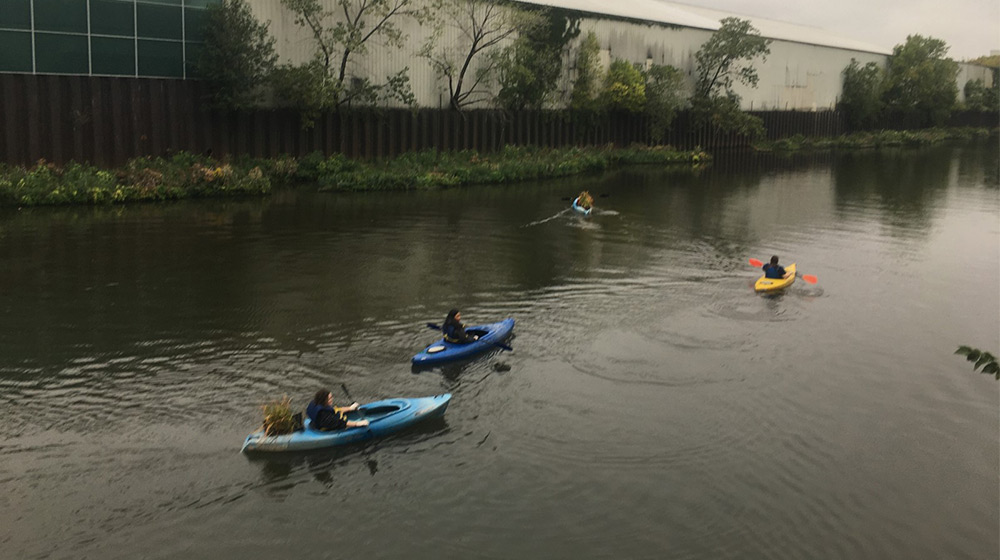 Three people kayak down a river on a cloudy day