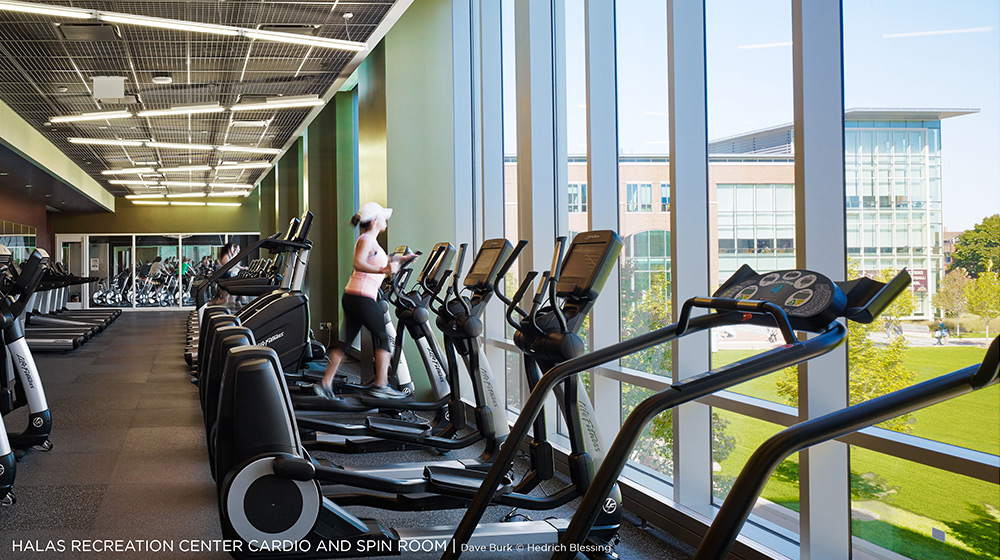 A long line of ellipticals are placed in front of large windows overlooking the campus of Loyola University Chicago