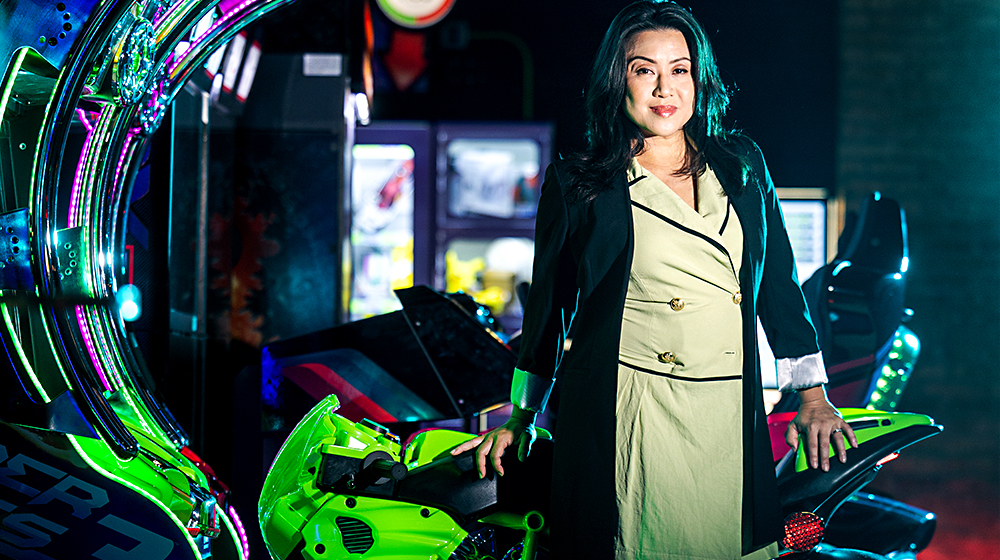 Florence Chee PhD, Loyola School of Communication professor and program director of the Center, stands near a game in a gaming arcade.