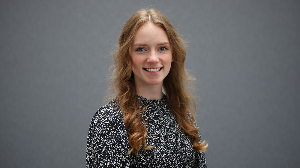 MVSS Benefits Coordinator Kimberly Davenport smiles for a headshot photo against a grey background wearing a black and white patterned shirt.