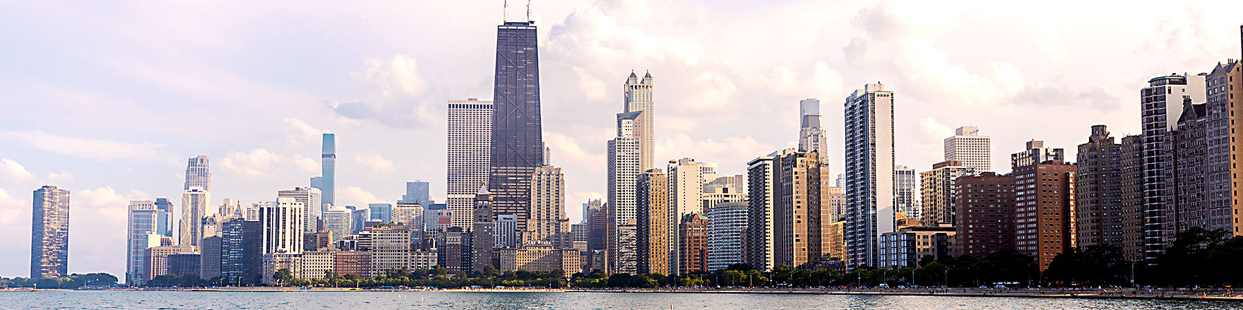 Chicago skyline with Lake Michigan in the foreground and a cloudy sky.